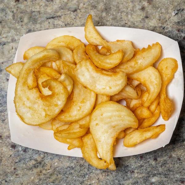 A white paper tray filled with golden-brown, crispy curly fries on a speckled countertop.