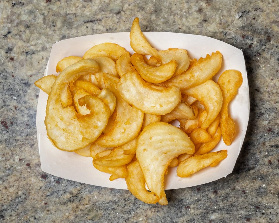 A white paper tray filled with golden-brown, crispy curly fries on a speckled countertop.