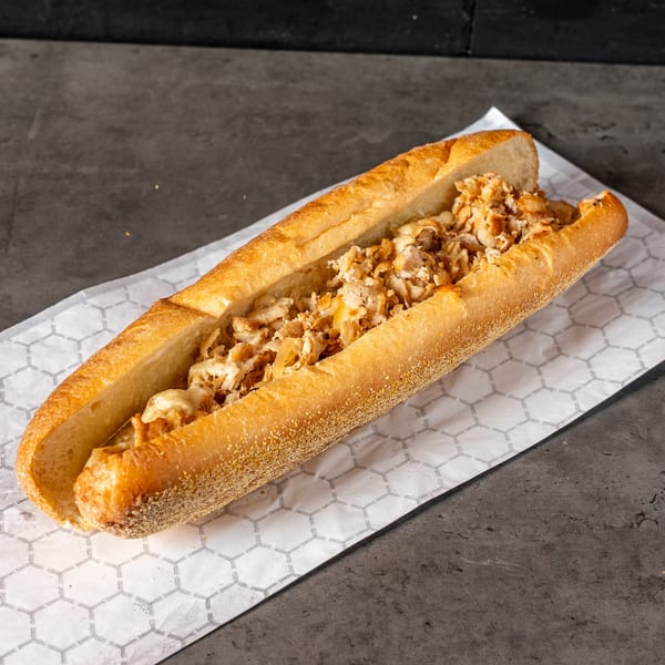 A chicken cheesesteak sandwich on a long roll, filled with chopped chicken and melted cheese.