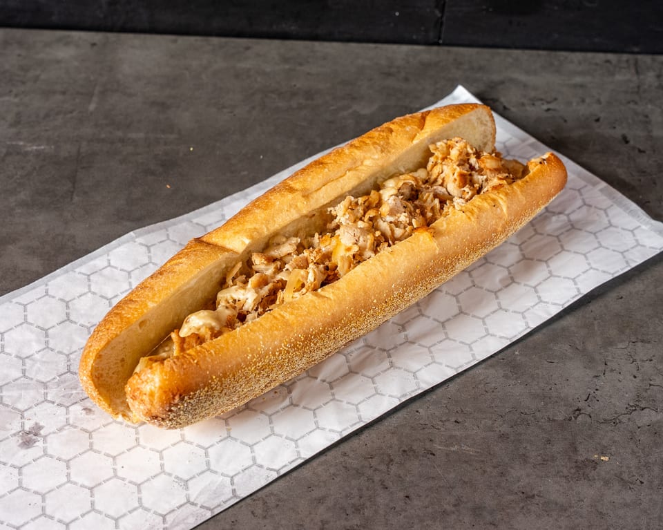 A chicken cheesesteak sandwich on a long roll, filled with chopped chicken and melted cheese.