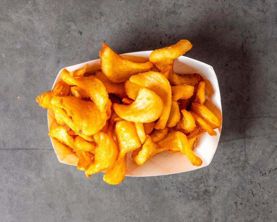 Golden curly fries in a white paper tray, viewed from directly above on a dark gray surface.