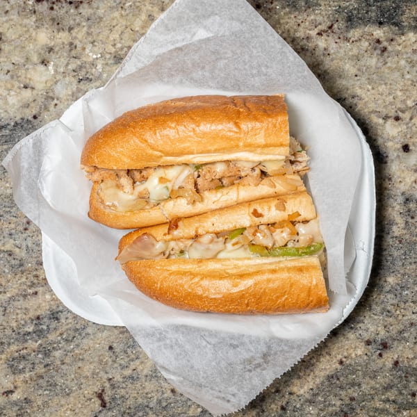 Two halves of a chicken cheesesteak sandwich with melted cheese, onions, and peppers.