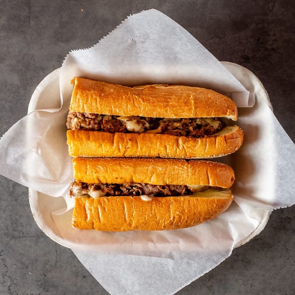 Two halves of a Philly cheesesteak sandwich with melted cheese and steak, served in a basket.