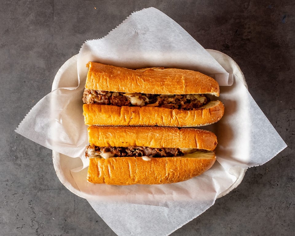 Two halves of a Philly cheesesteak sandwich with melted cheese and steak, served in a basket.
