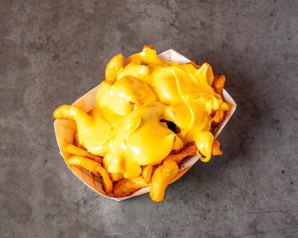 Golden french fries generously covered in melted yellow cheese sauce, served in a paper tray.
