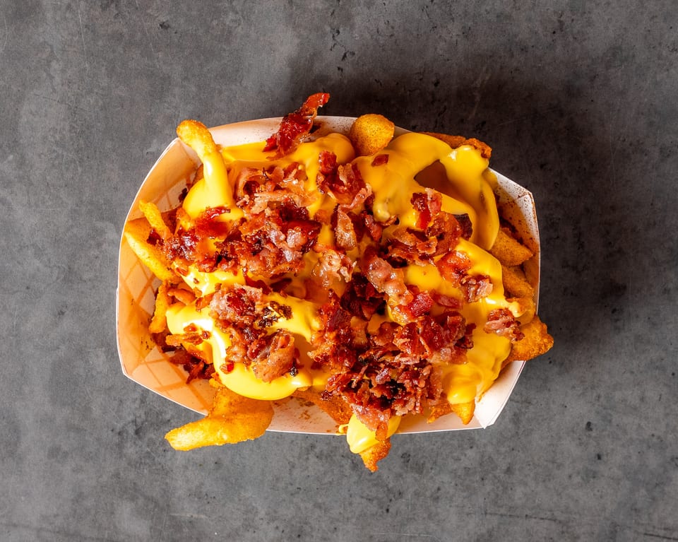 Overhead view of a basket of golden french fries smothered in melted cheese and crispy bacon bits.