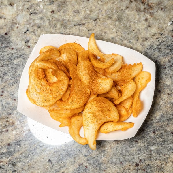 A white paper tray filled with golden-brown seasoned potato chips on a speckled countertop.