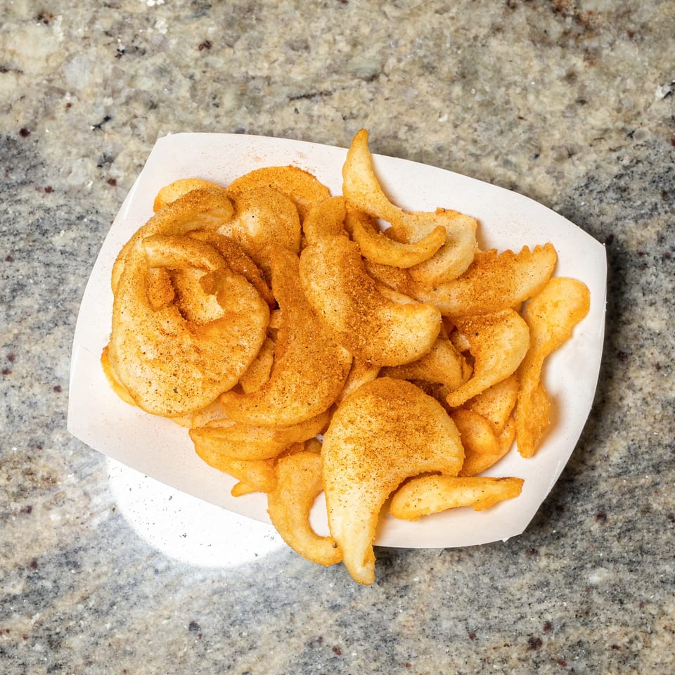 A white paper tray filled with golden-brown seasoned potato chips on a speckled countertop.