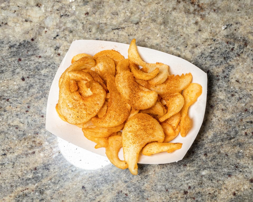 A white paper tray filled with golden-brown seasoned potato chips on a speckled countertop.