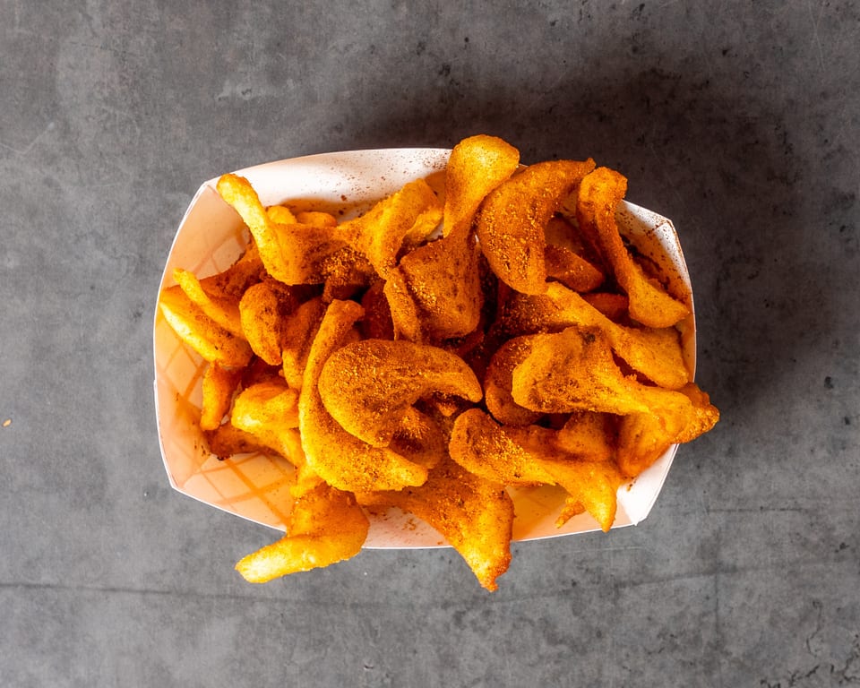 Top-down view of a white paper tray filled with golden-brown, seasoned curly fries on a dark gray surface.