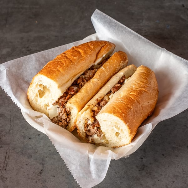 Three sections of a cheesesteak sandwich with meat, onions, and cheese in a white paper-lined basket.