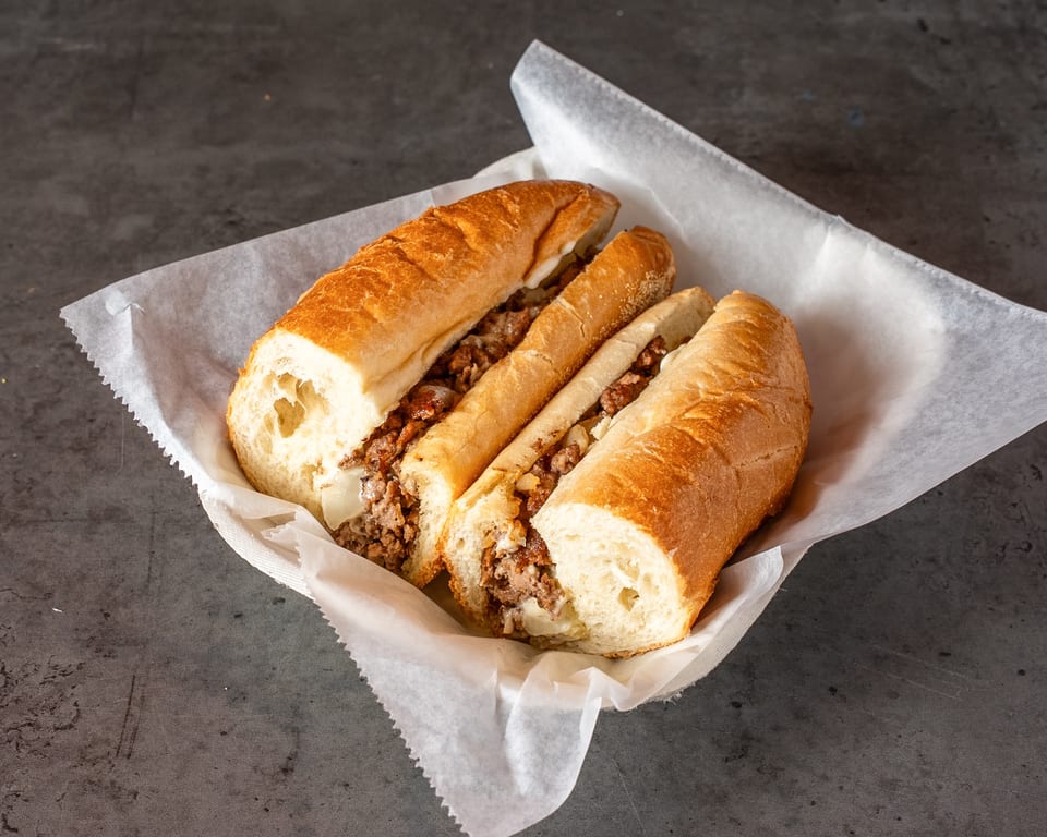Three sections of a cheesesteak sandwich with meat, onions, and cheese in a white paper-lined basket.