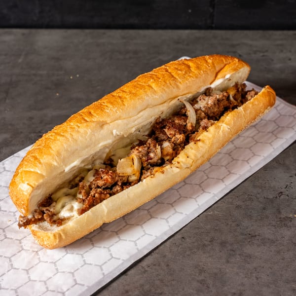 A delicious cheesesteak sandwich with melted cheese, meat, and onions on a white paper.