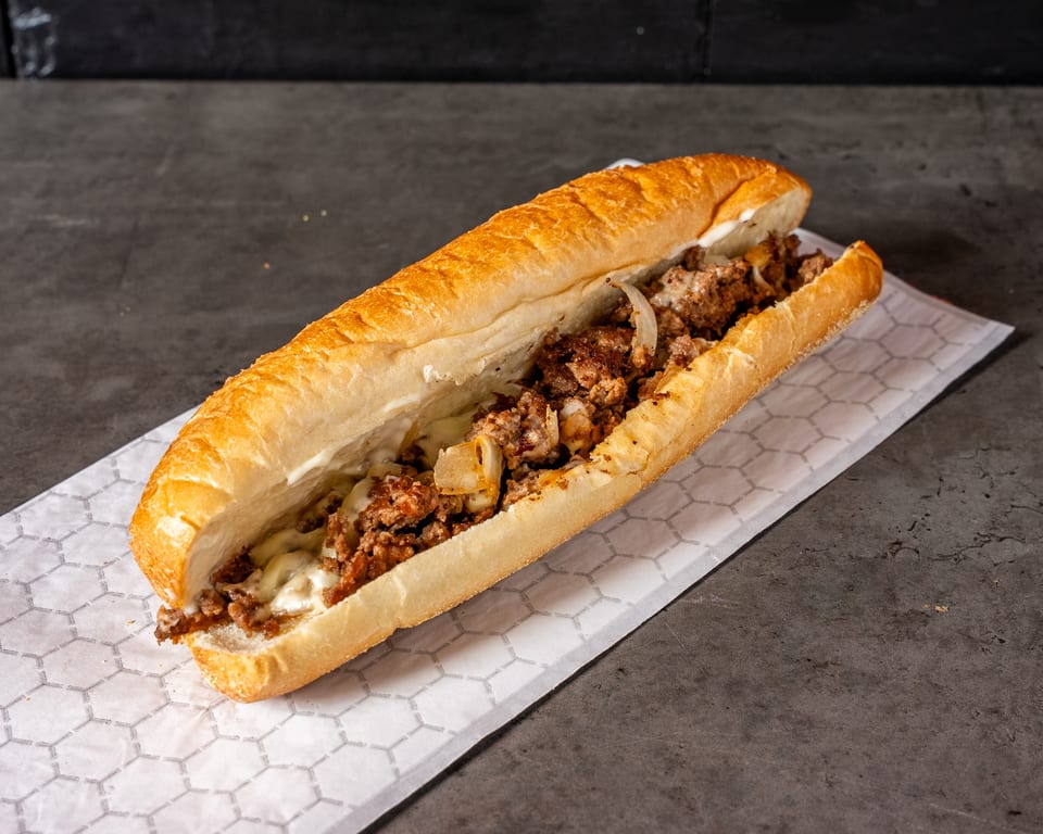 A delicious cheesesteak sandwich with melted cheese, meat, and onions on a white paper.