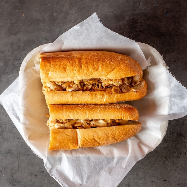Two halves of a chicken cheesesteak sandwich with onions in a paper-lined basket.