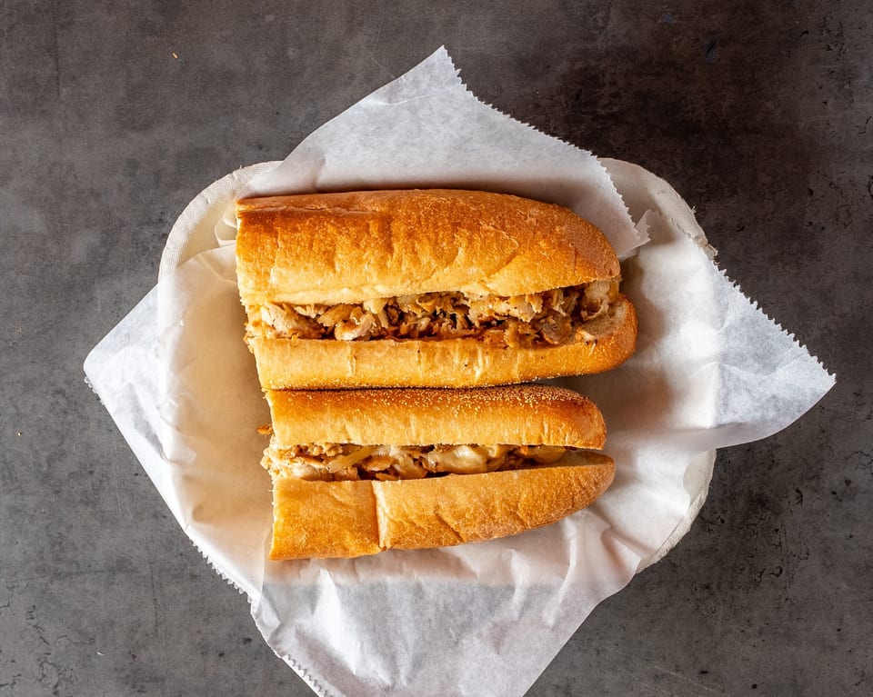Two halves of a chicken cheesesteak sandwich with onions in a paper-lined basket.
