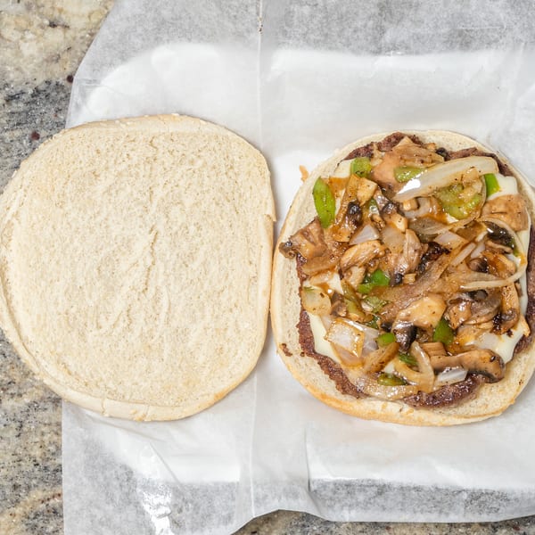 Open-faced burger with melted cheese, sautéed mushrooms, onions, and green peppers on a bun.