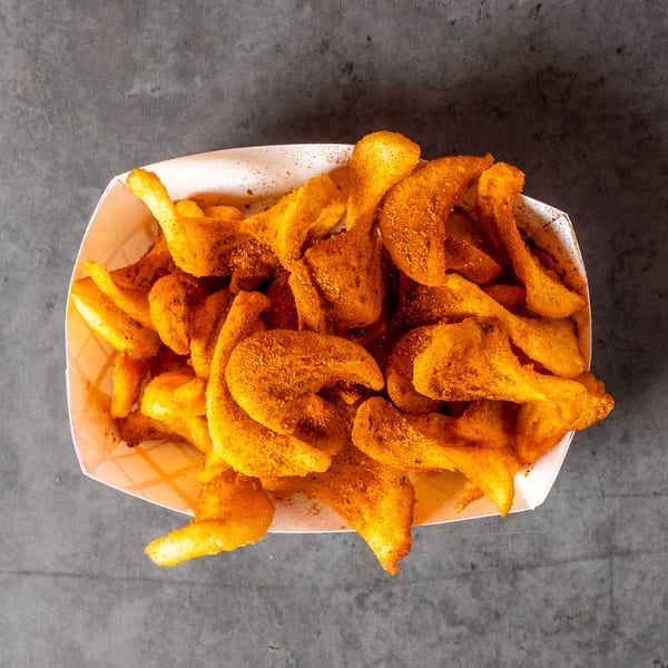 Top-down view of a white paper tray filled with golden-brown, seasoned curly fries on a dark gray surface.