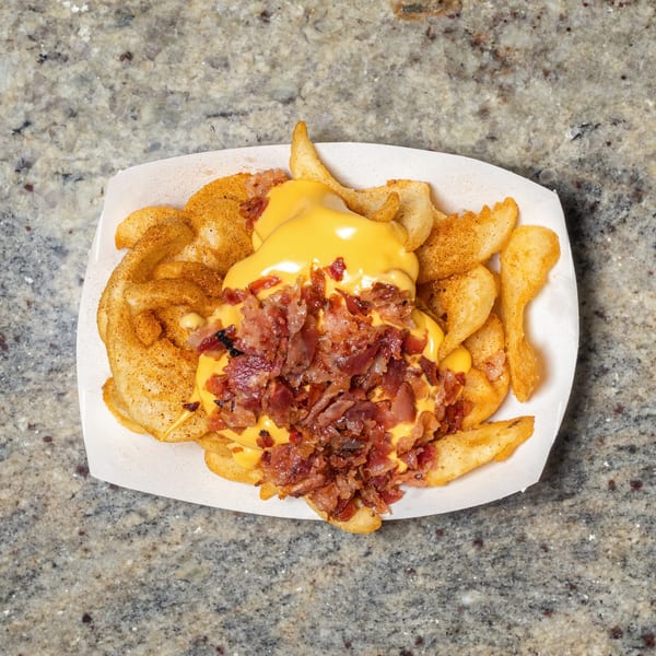 Seasoned potato wedges topped with melted cheese and crispy bacon bits in a white paper tray.