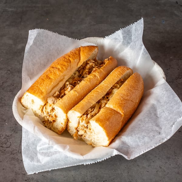 Three chicken cheesesteak sandwiches in a basket lined with white paper on a dark surface.