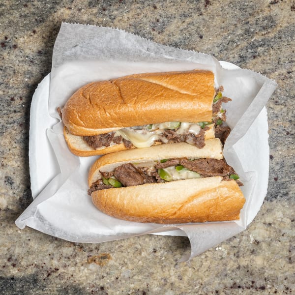 Two cheesesteak sandwiches with melted cheese, green peppers, and onions on a white plate.