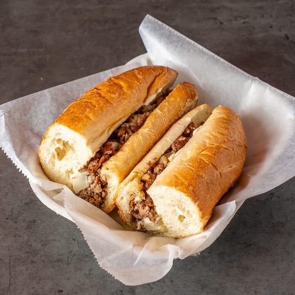 Two halves of a cheesesteak sandwich with meat, onions, and melted cheese in a paper-lined basket.