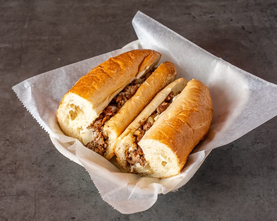 Two halves of a cheesesteak sandwich with meat, onions, and melted cheese in a paper-lined basket.