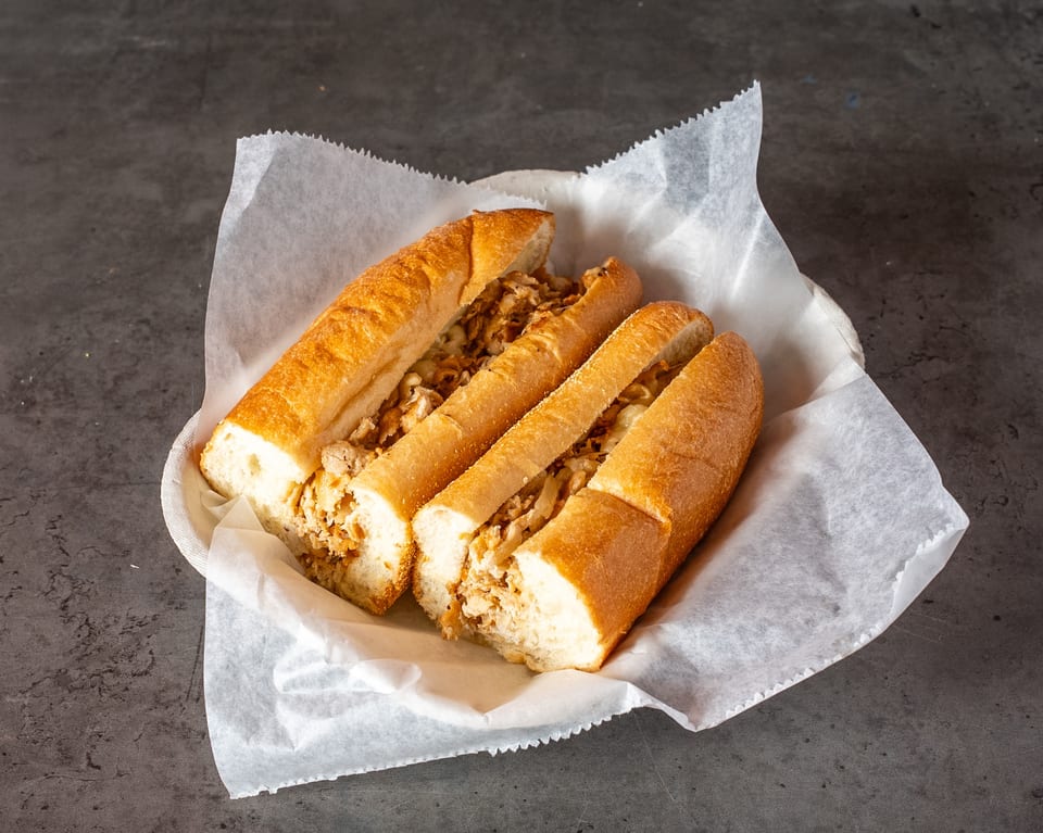 Three chicken cheesesteak sandwiches in a basket lined with white paper on a dark surface.