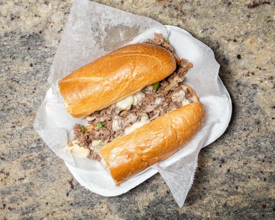 A delicious cheesesteak sandwich with melted cheese, meat, and peppers on a hoagie roll.
